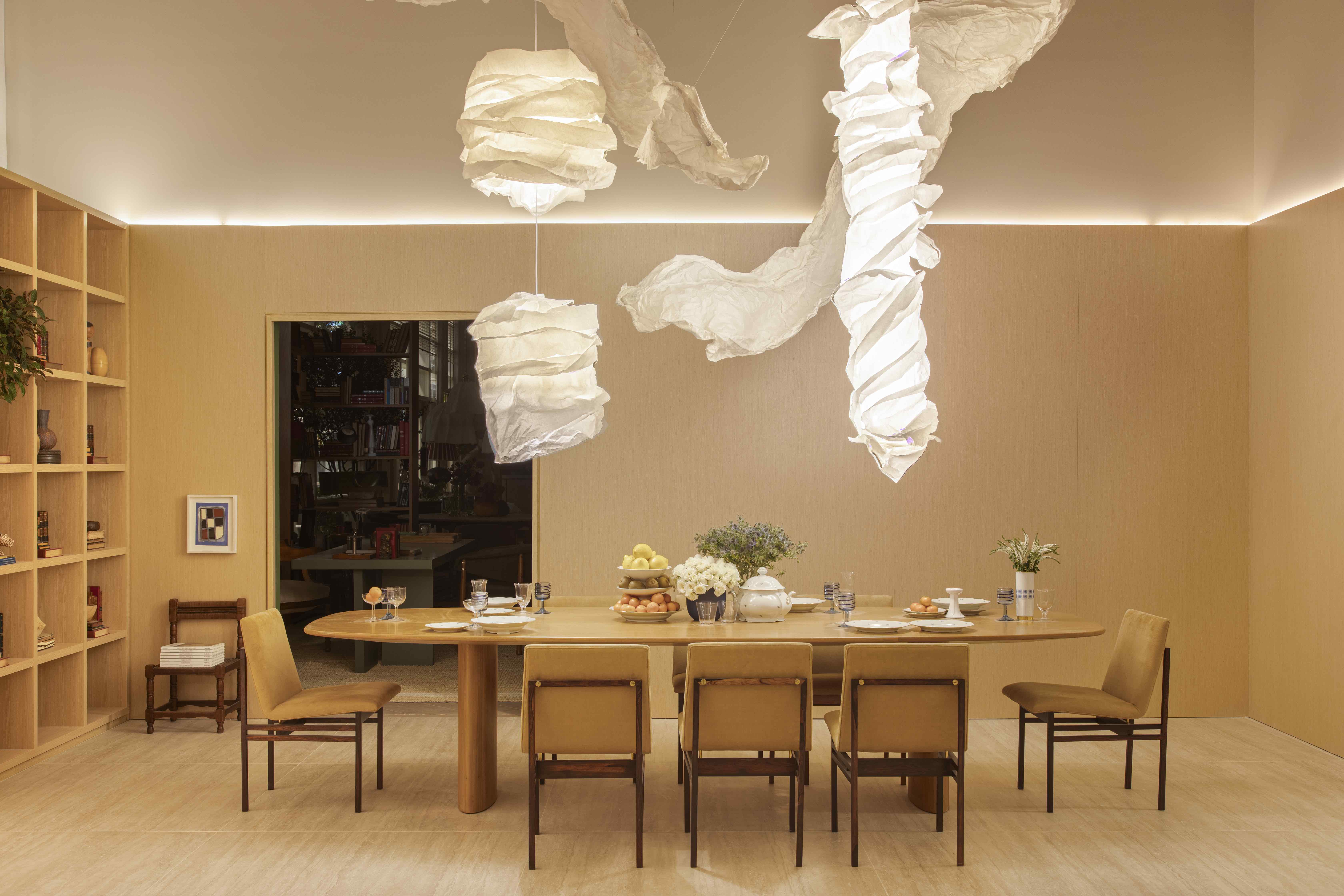 Da Hora Arquitetura - Loft Vastu. Projeto da CASACOR São Paulo 2023. Na foto, sala de jantar com luminária orgânica, estante de madeira e pé-direito duplo.