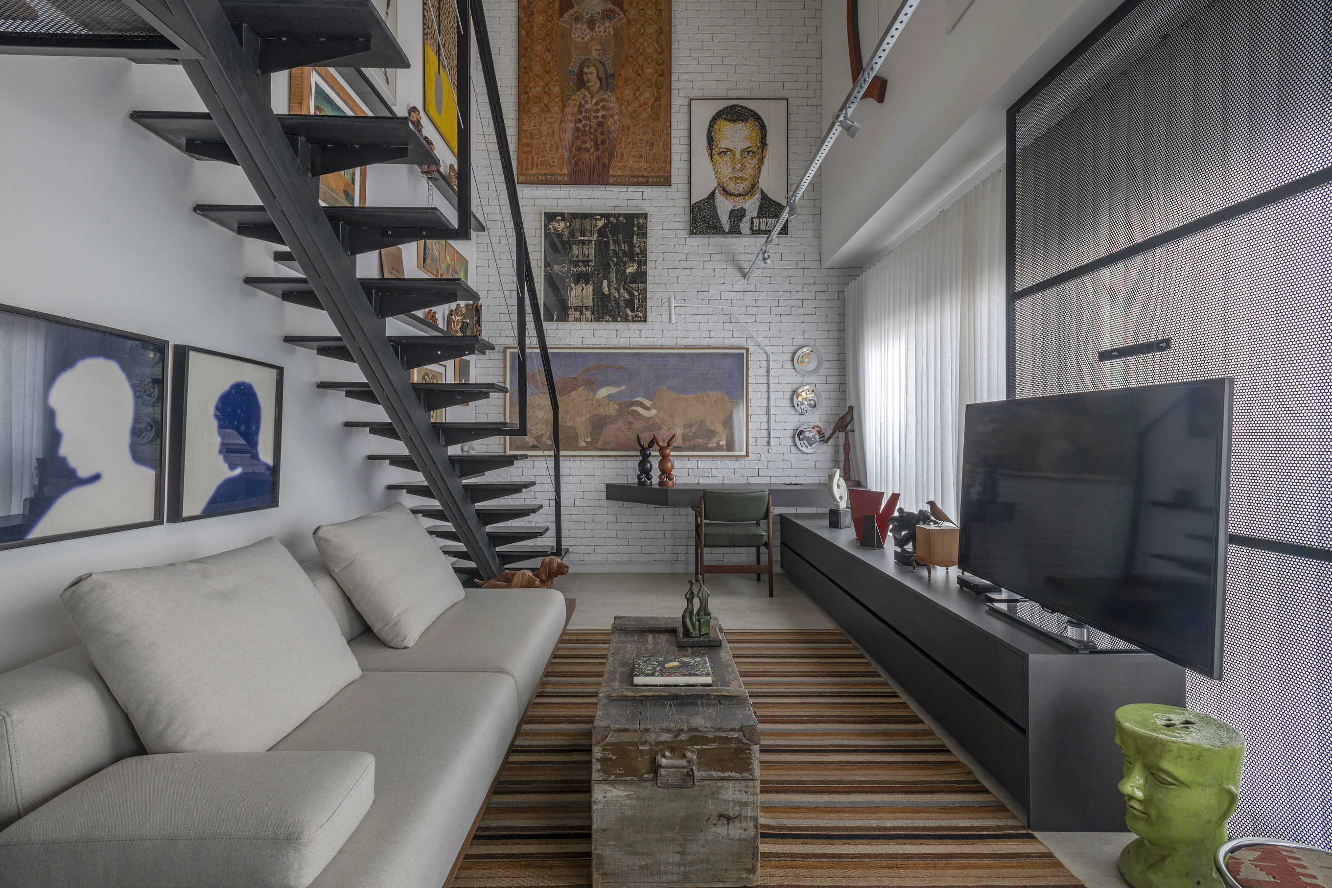 Loft de 64 m² ganha décor industrial e coleção de arte dos moradores. Projeto de Junior Piacesi. Na foto, escada com gallery wall na parede. Sala de estar com tapete listrado.