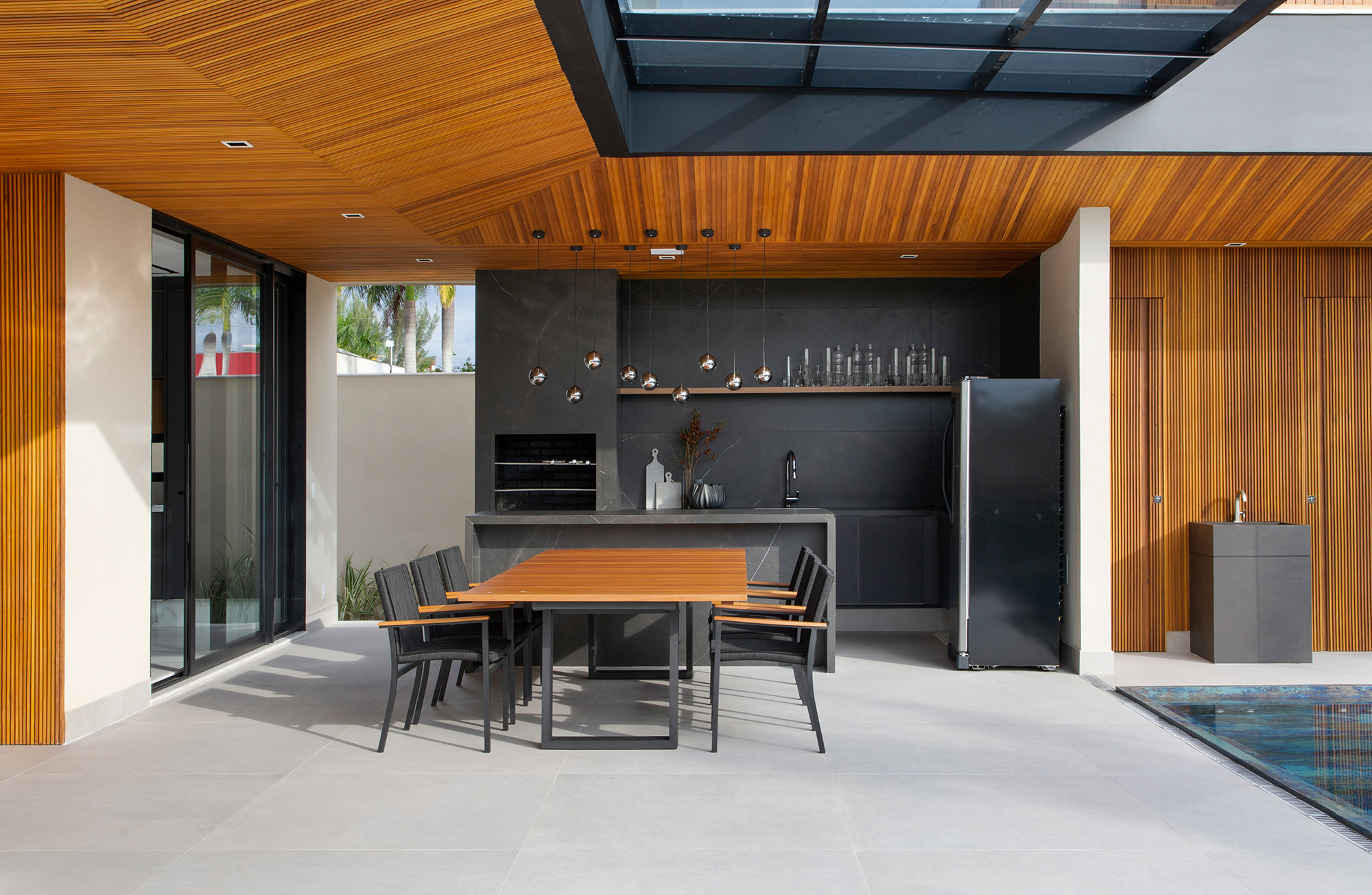 Painéis de madeira e estilo minimalista dão o tom desta casa de 780 m². Projeto de Hannah Cabral e Monique Pampolha. Na foto, varanda gourmet com piscina e churrasqueira,