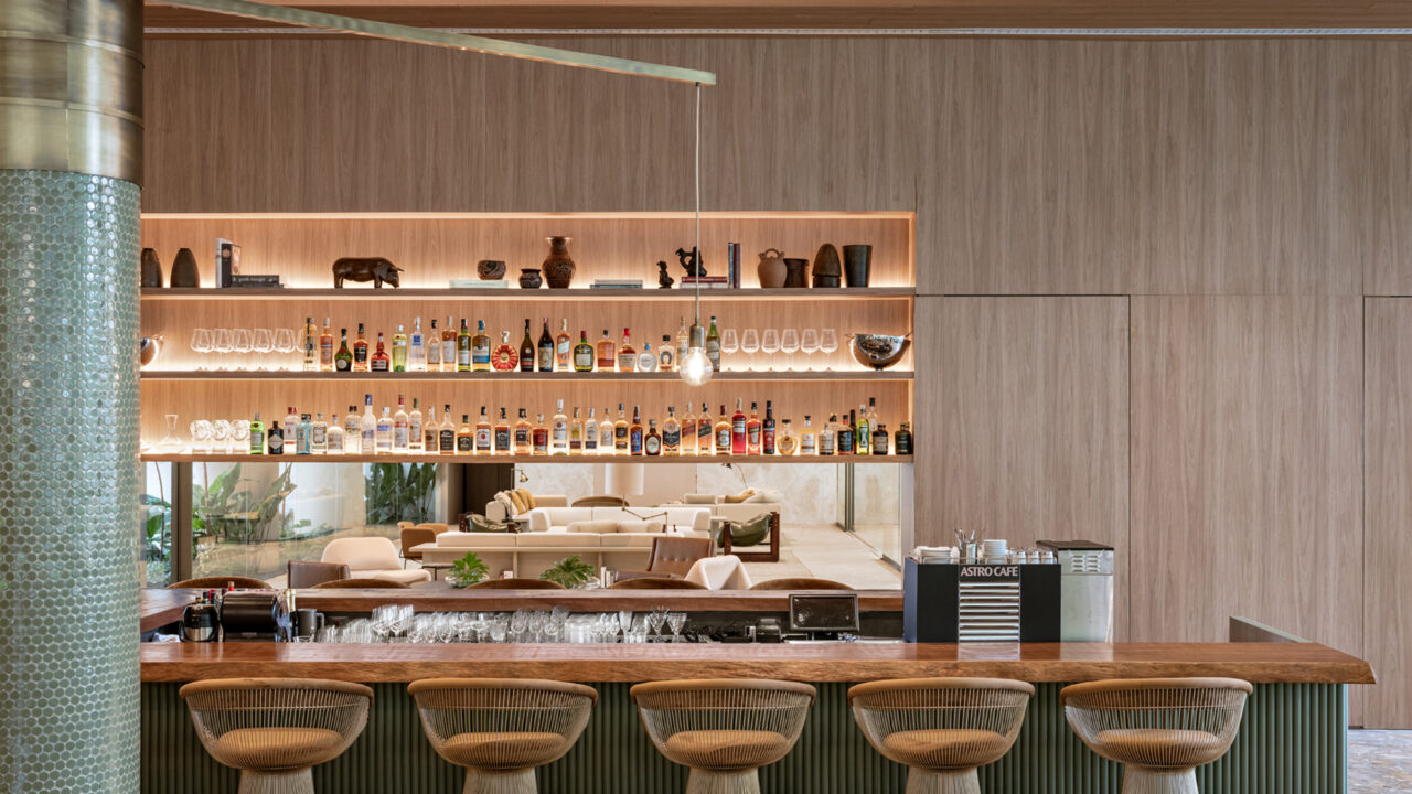 Studio Arthur Casas assina arquitetura e interiores de hotel de luxo em SP. Na foto, bar com estante iluminada e parede de madeira.