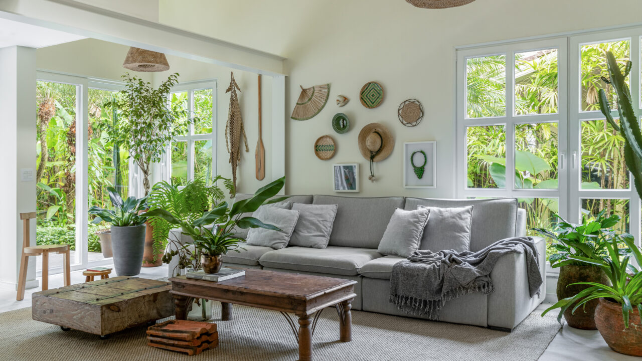 Casa de praia repleta de plantas se integra à mata nativa do entorno. Projeto de Ricardo Abreu. Na foto, sala com vista para o jardim e sofá cinza.