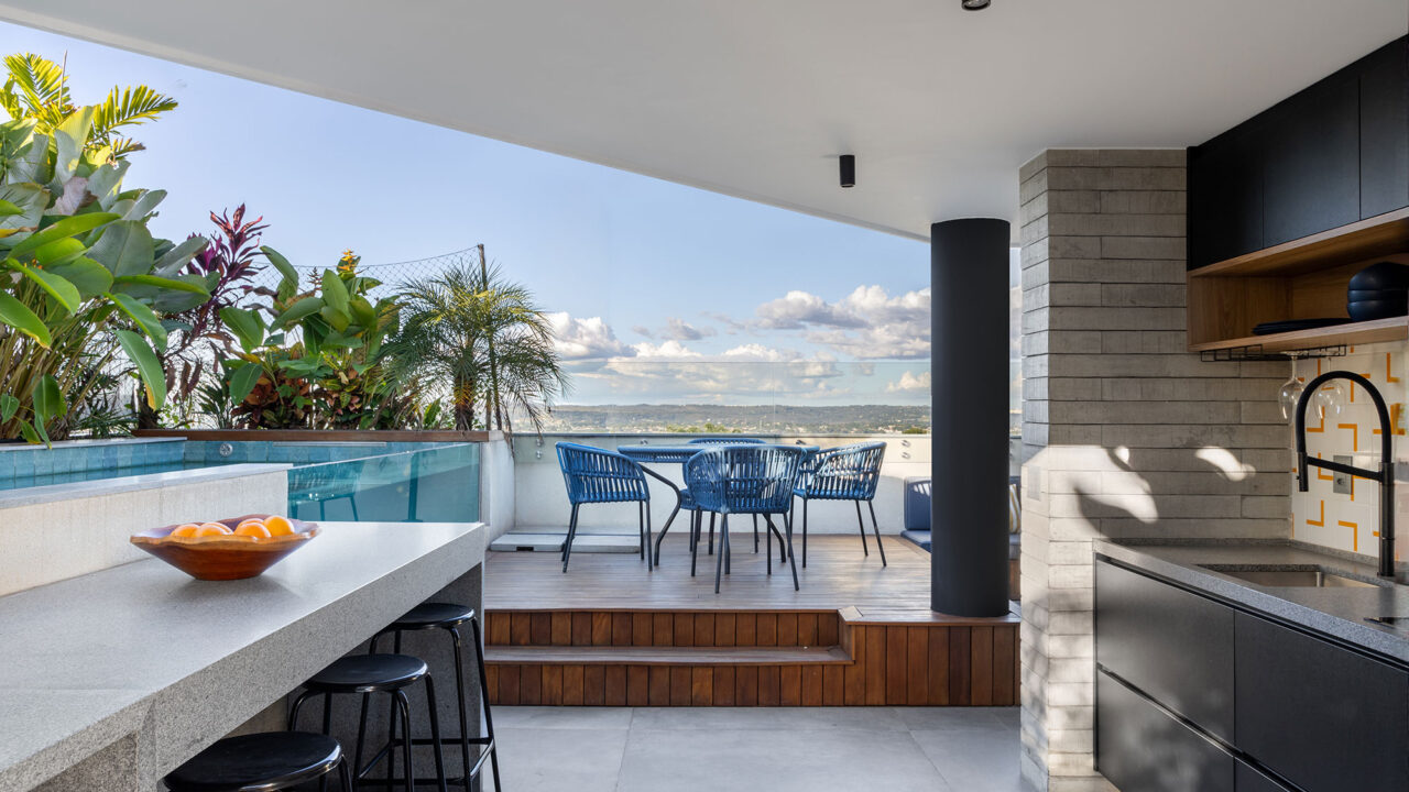 Dúplex industrial de 290 m² une piscina de vidro e área para ver jogos. Projeto Morada 31.12. Na foto, área gourmet com deque de madeira, azulejo colorido e churrasqueira.