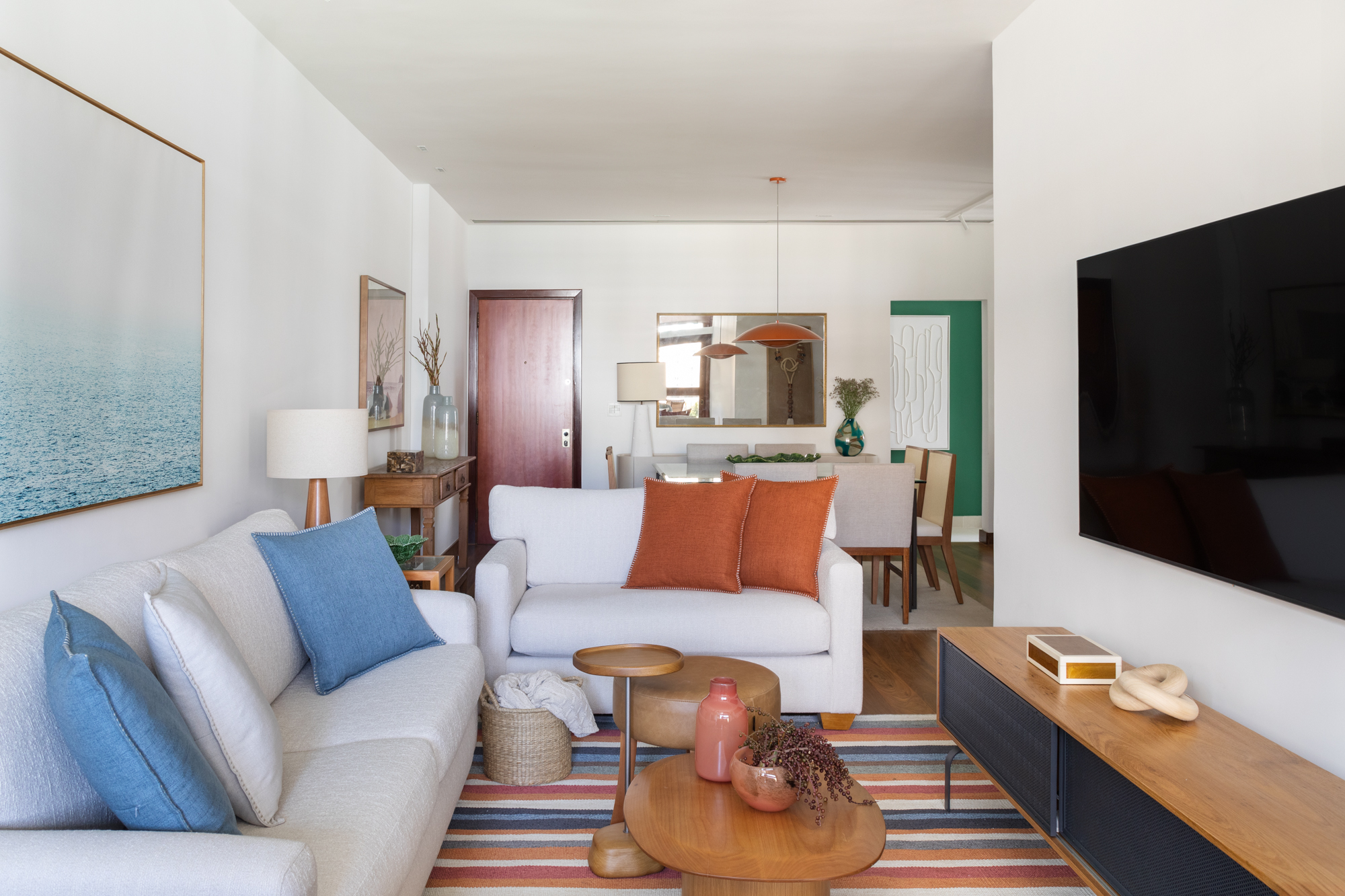 Apartamento à beira-mar ganha cara de casa com cozinha verde. Projeto de Vivian Reimers. Na foto, sala de estar com tapete listrado, tv e quadros.