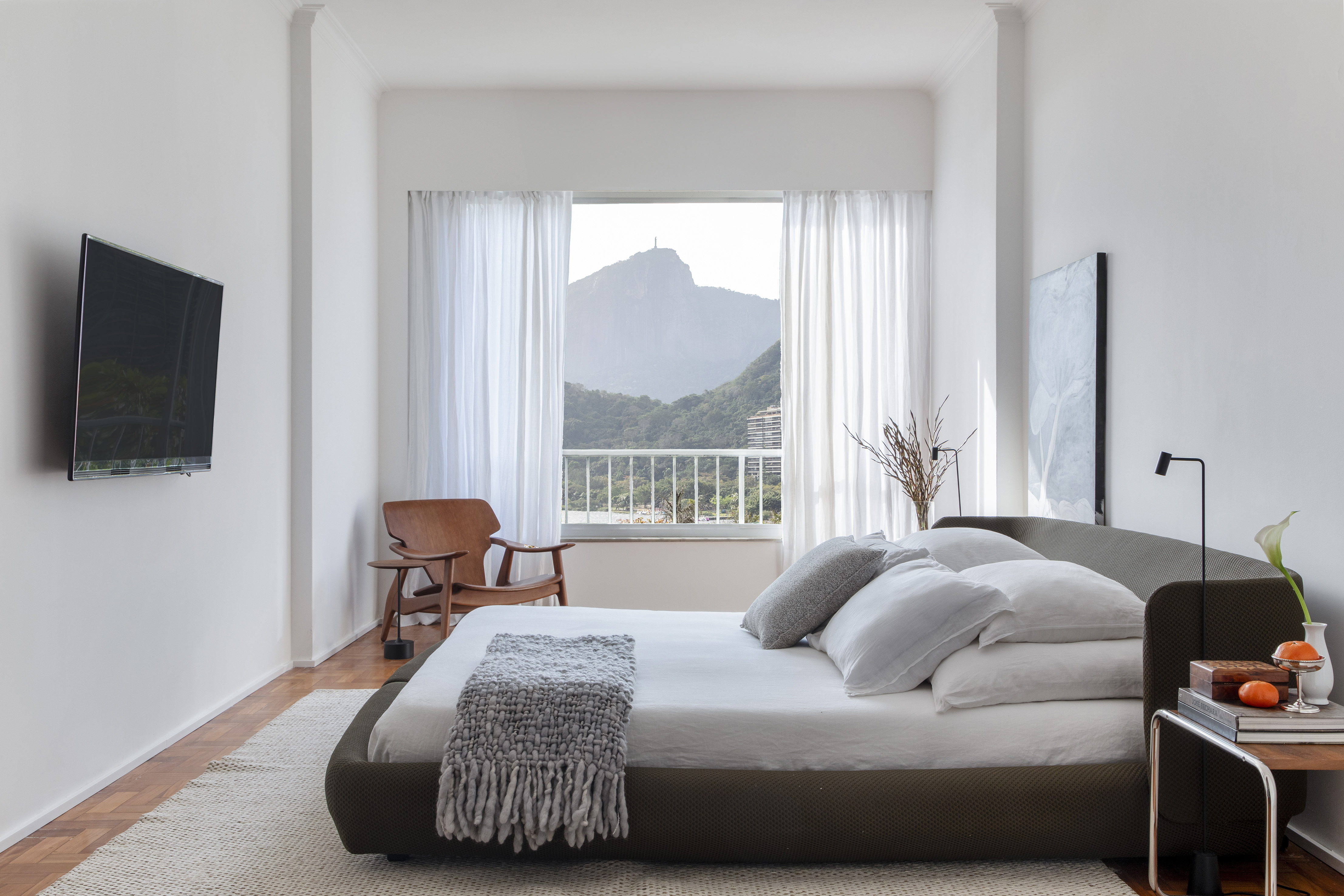 Apartamento possui vista para quatro cartões postais do Rio de Janeiro. Projeto de João Panaggio. Na foto, quarto com cama, quadro e mesa de cabeceira.