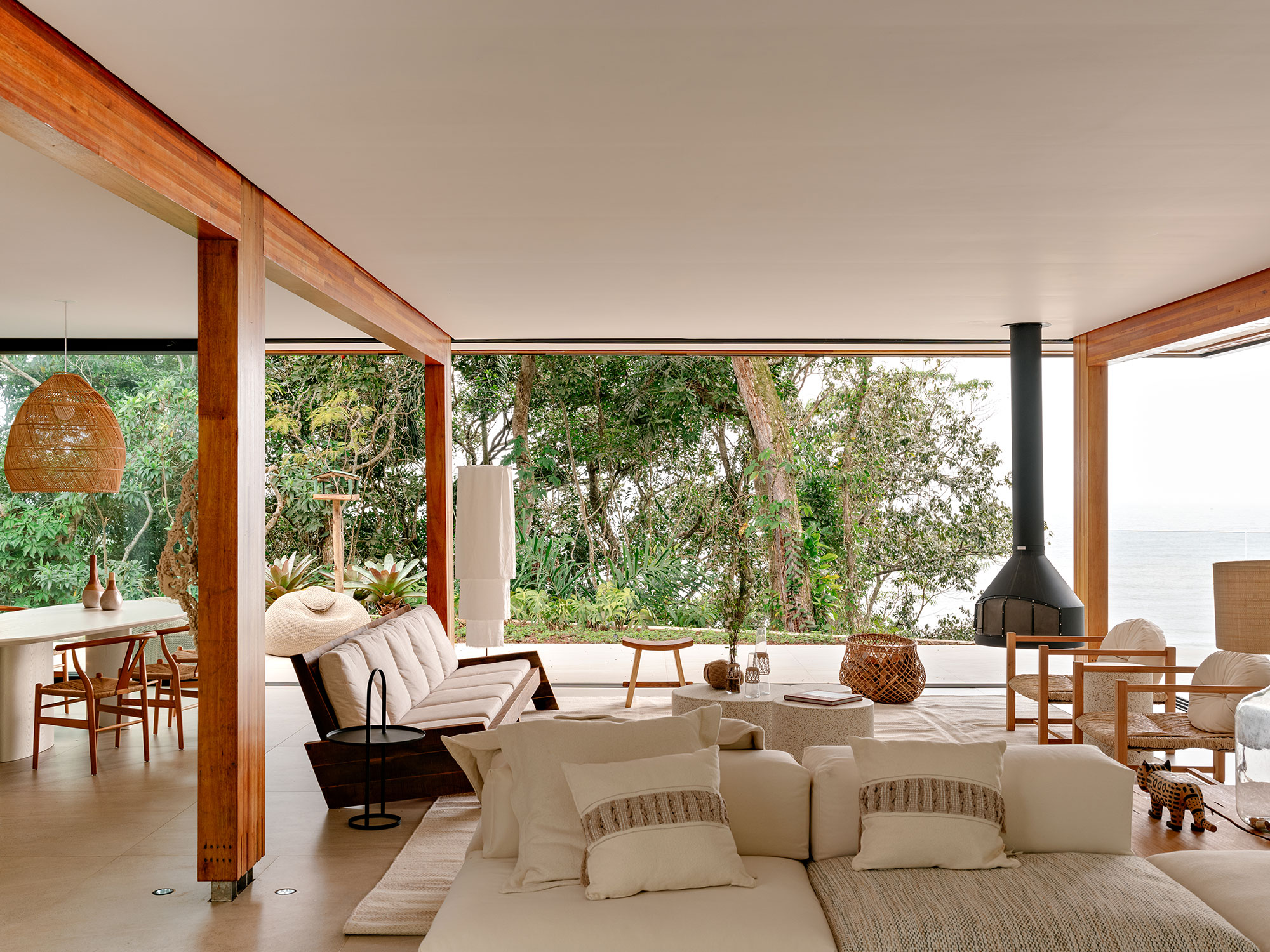 Casa de praia sustentável vira refúgio no meio da Mata Atlântica. Projeto de Patrícia Martinez. Na foto, sala com pano de vidro e poltronas e lareira.