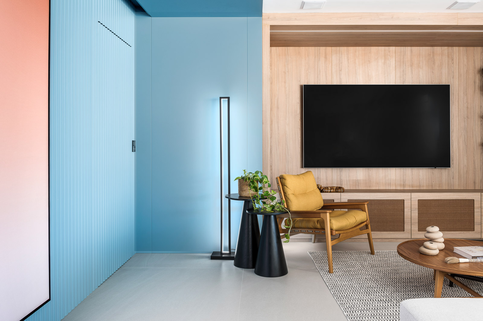 Amarelo mostarda e azul dão personalidade a apartamento de 227 m². Projeto de Tetriz Arquitetura. Na foto, sala com parede azul e tv.