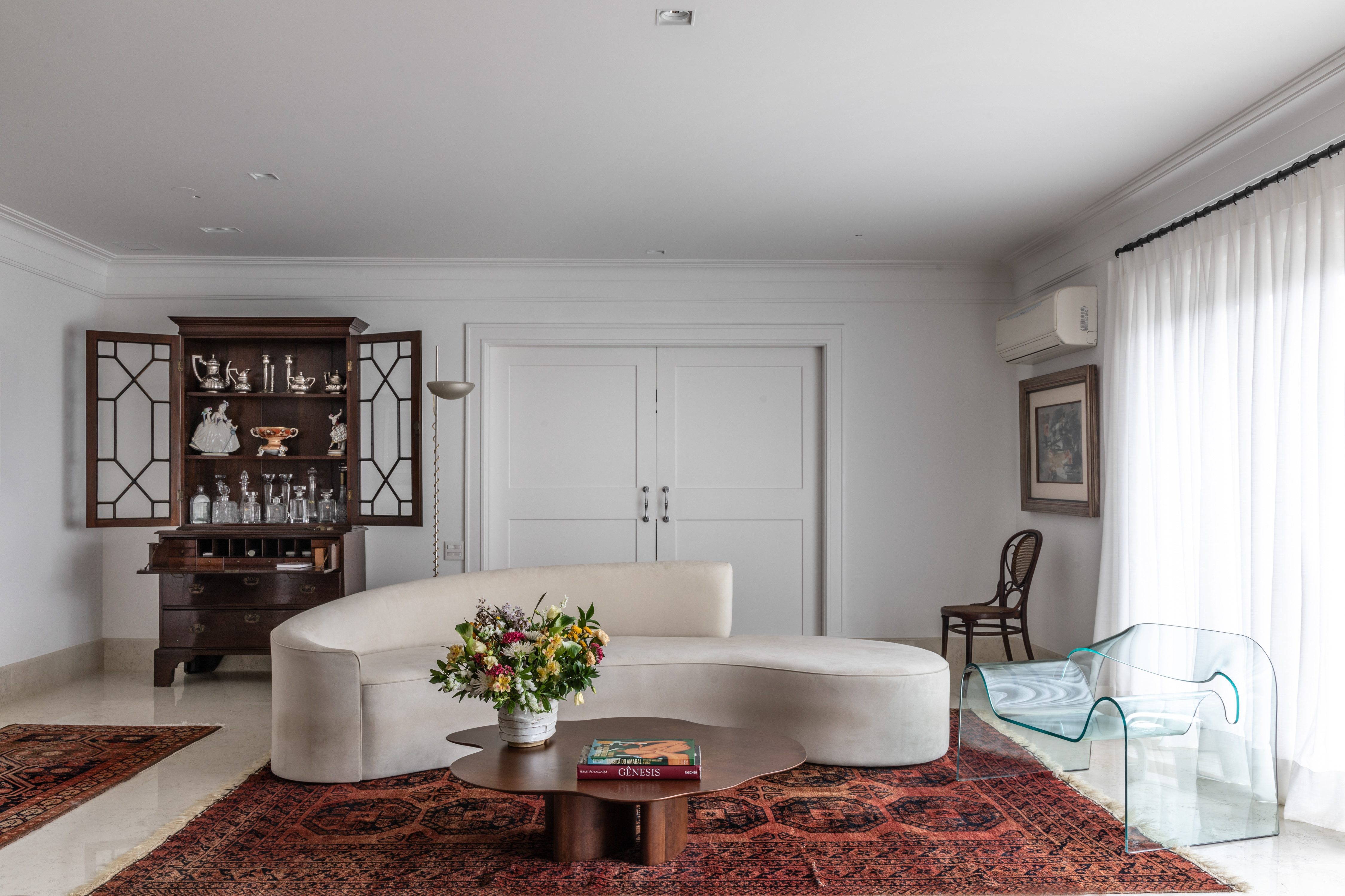 Com amplo jardim, apê de 650 m² mescla referências francesas e brasileiras. Projeto de Felipe Carolo. Na foto, sala com sofá branco curvo.