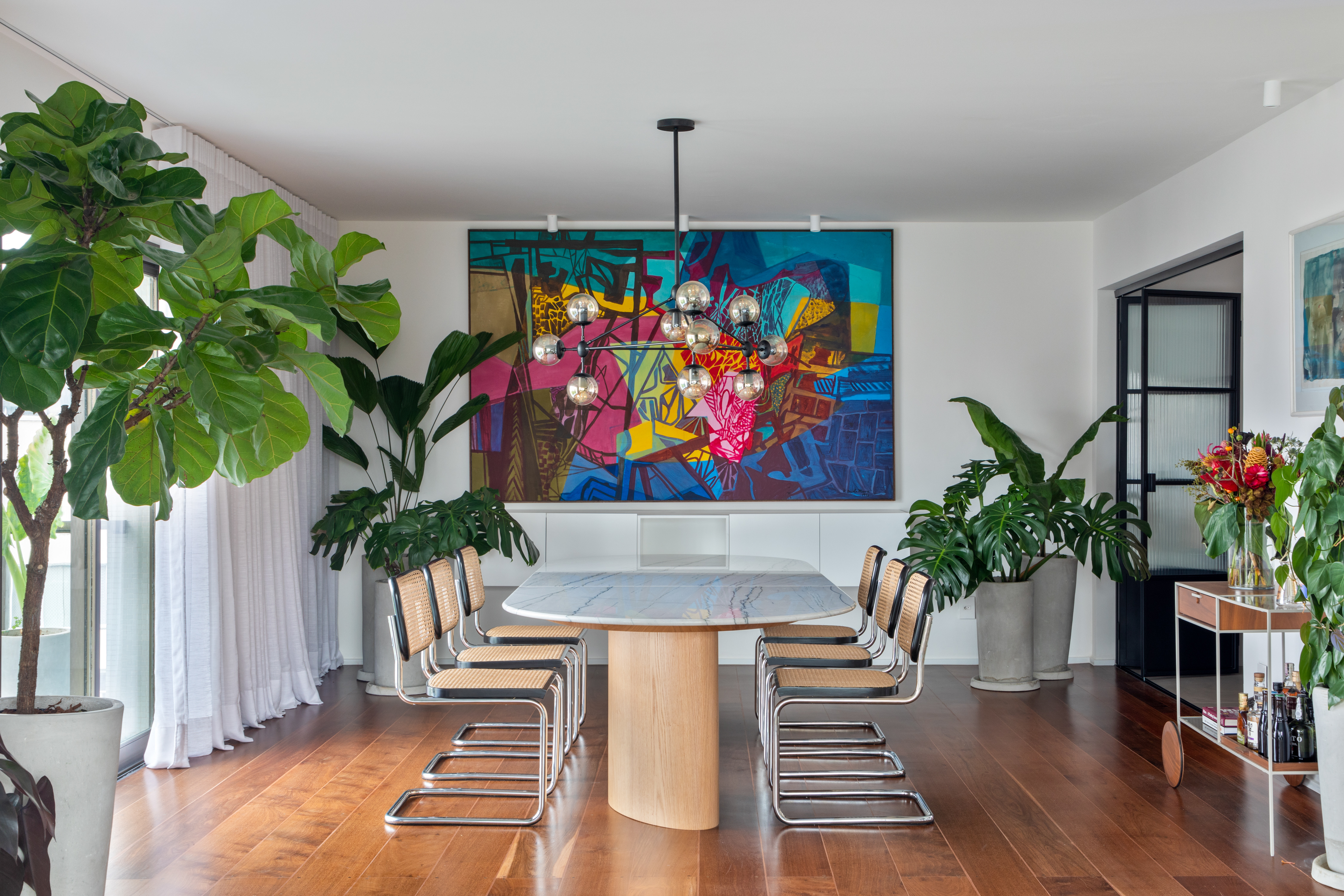 Obras de arte e revestimentos conferem cor a projeto de 300 m². Projeto de Rodra Arquitetura, Na foto, sala de jantar com plantas e quadro.