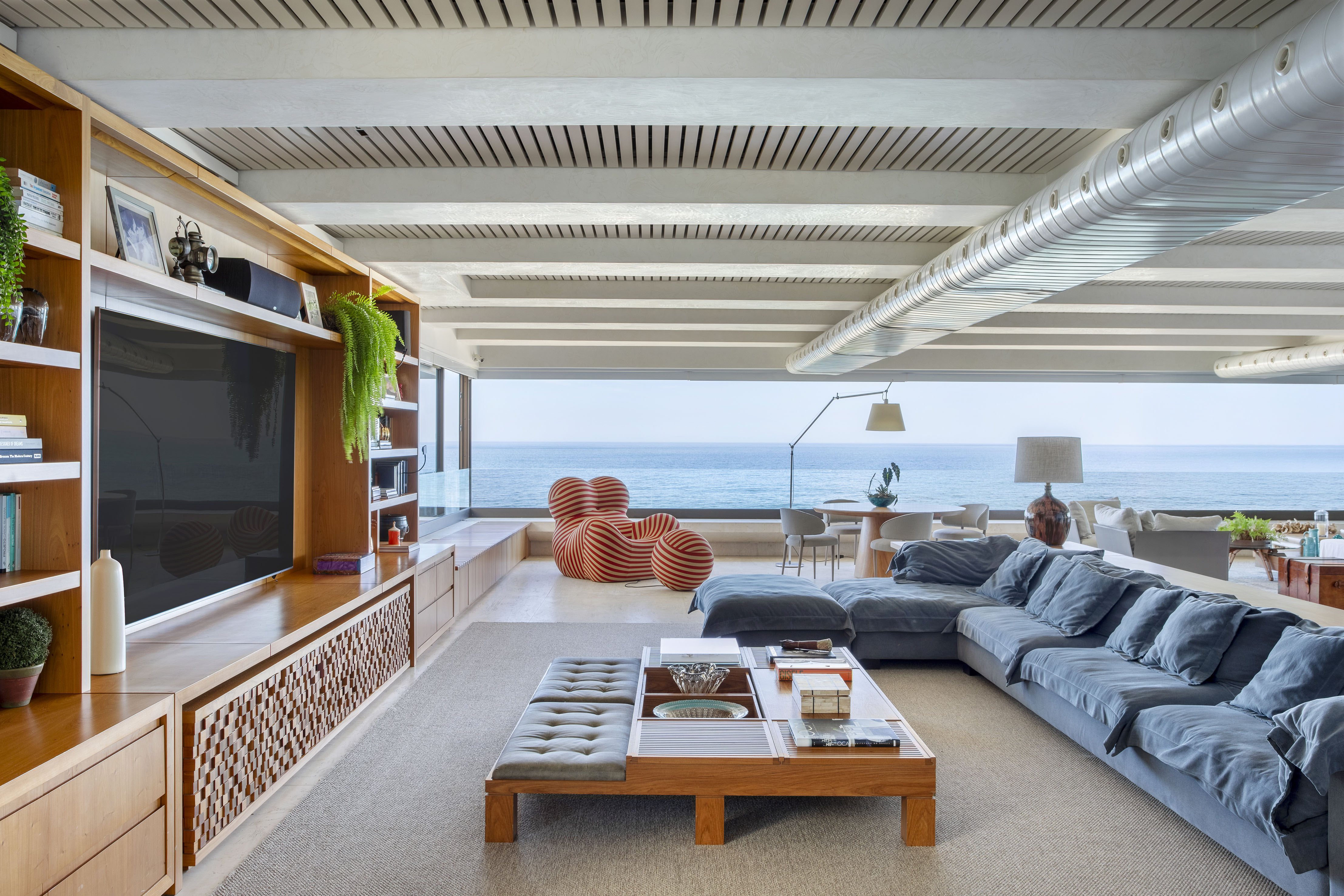 Com vista 180º do mar, apartamento de 550 m² ganha projeto jovem e solar. Projeto de 021 Arquitetura. Na foto, sala com vista para o mar, poltrona e teto ripado.