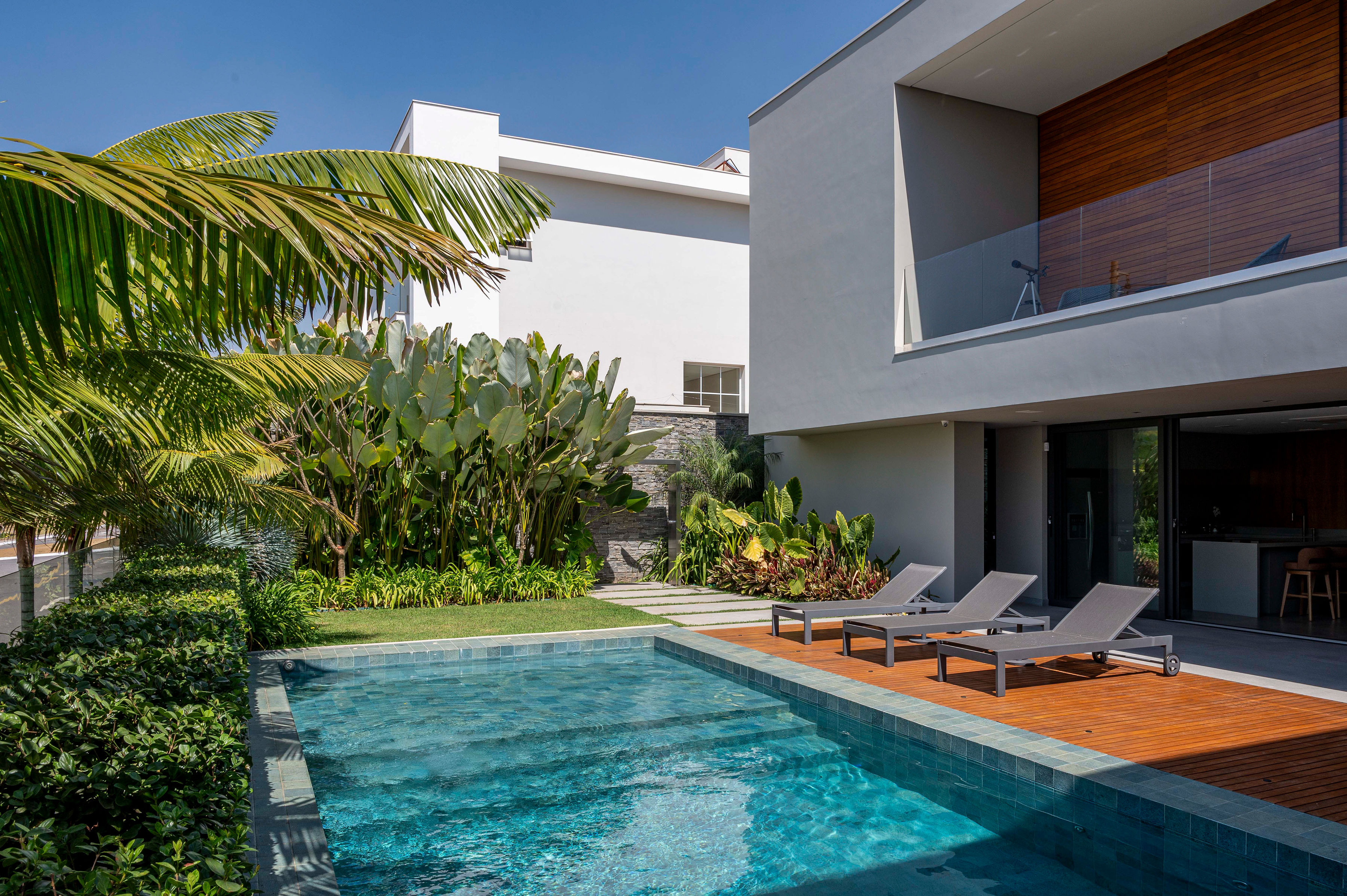 Casa de esquina ganha paisagismo com 24 espécies tropicais. Projeto de Flávia D'Urso. Na foto, piscina, deque e paisagismo.