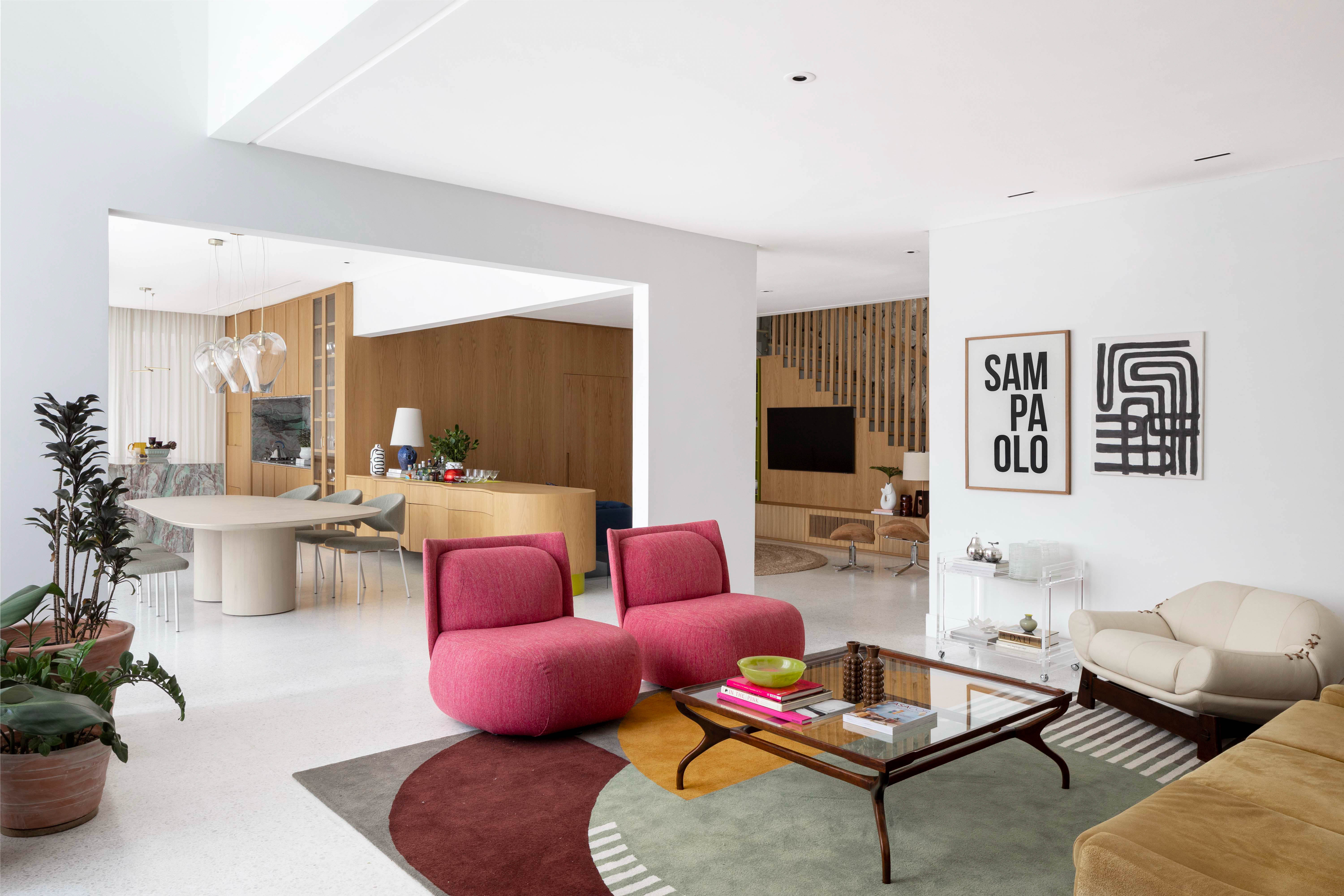 Moderna, pop e fun: casa reúne cores vibrantes e esconderijo sob escada. Projeto de Ana Weege. Na foto, sala de estar com quadros e poltronas cereja.