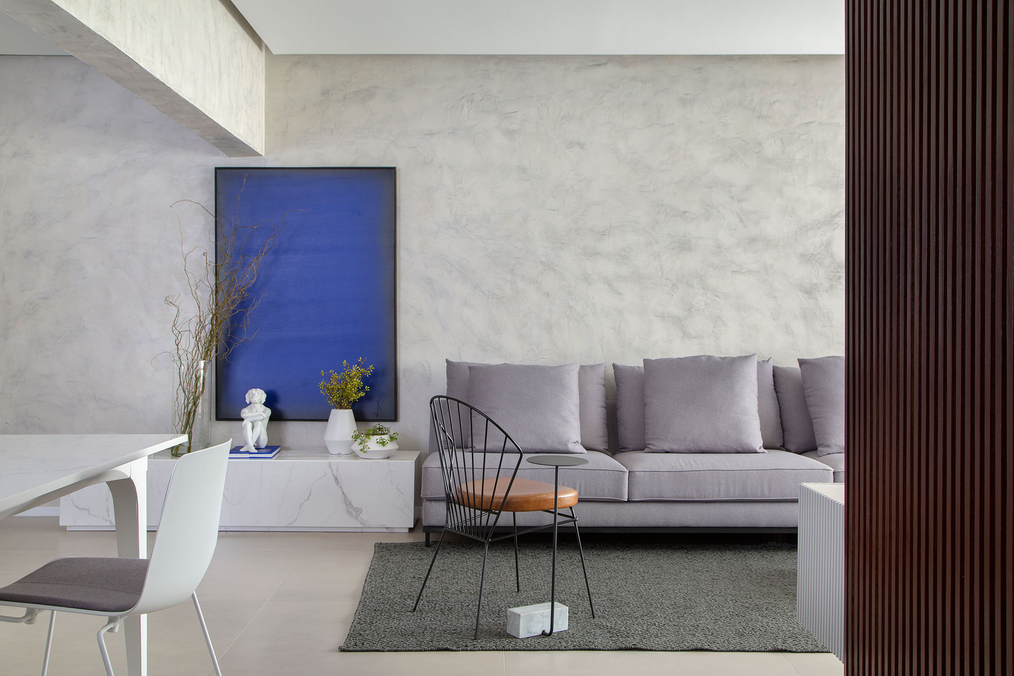 Espaços híbridos e conectados marcam apê com toques brutalistas. Projeto de Anna Fadul e Gregory Copello. Na foto, sala de estar com parede cinza e quadro.
